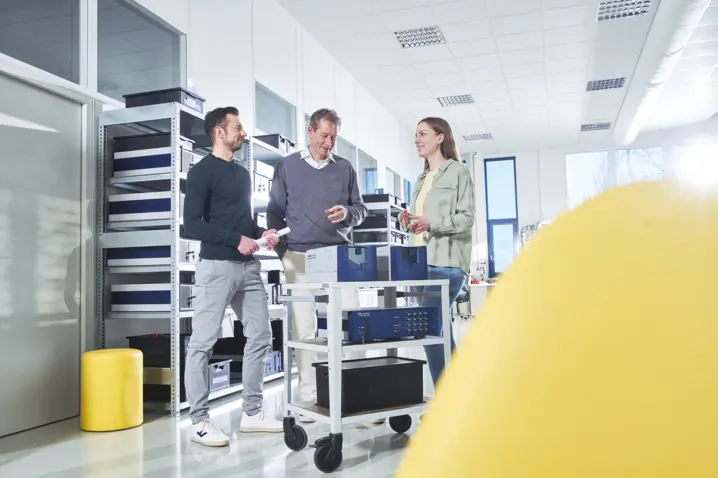 Three professionals discussing optical measurement equipment in a bright, modern laboratory at Polytec.