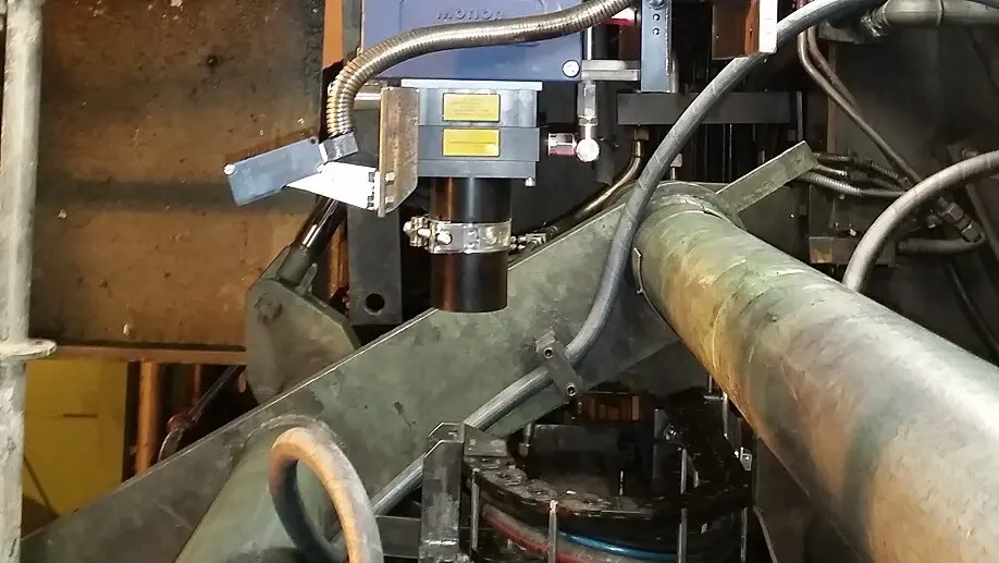 Polytec laser surface velocimeter mounted on industrial machinery measuring speed on a metal pipe in a factory setting.