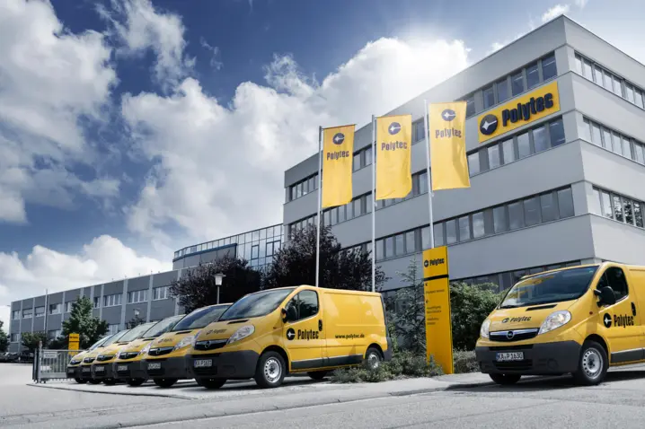 Polytec headquarters with branded yellow company vans and flags under a partly cloudy sky, showcasing optical measurement technology.