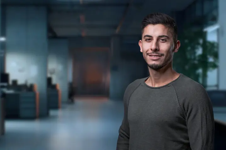 Confident young man smiling in a modern office environment, symbolizing professional service and support teams.