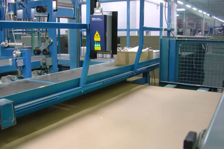 Blue automated laser sensor system measuring cut-to-length of cardboard on a production line for precise packaging control.