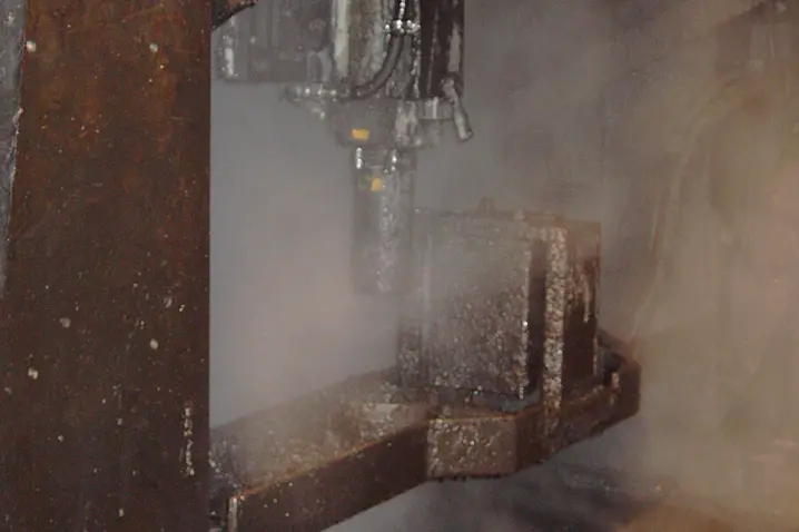 Rusty industrial metal machinery operating with steam or smoke in a manufacturing environment.