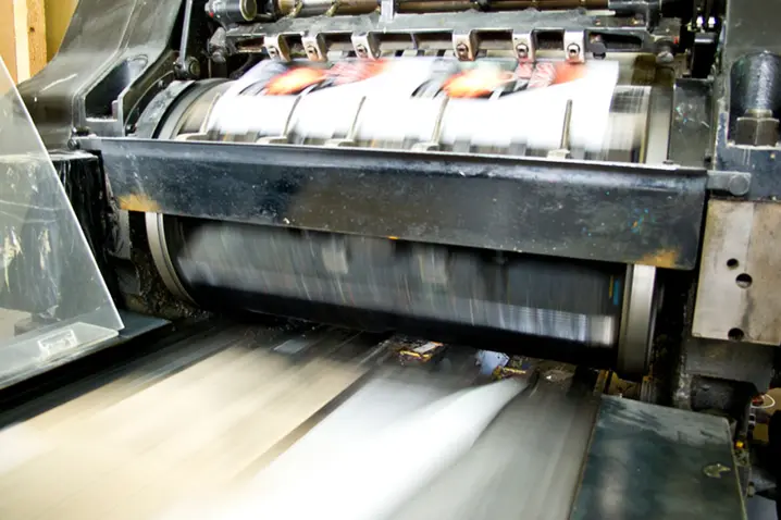 High-speed industrial printing press in motion producing fast-moving printed sheets for paper packaging manufacturing.