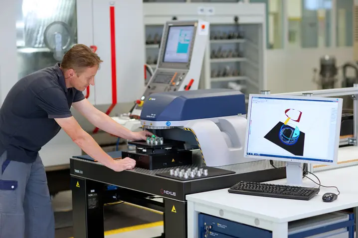 Technician operating an advanced optical 3D surface profiler with measurement data visible on computer screen in a lab.